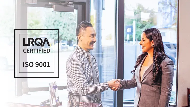 image of 2 people shaking hands in an office with a logo for the LRQA Certification for ISO 9001